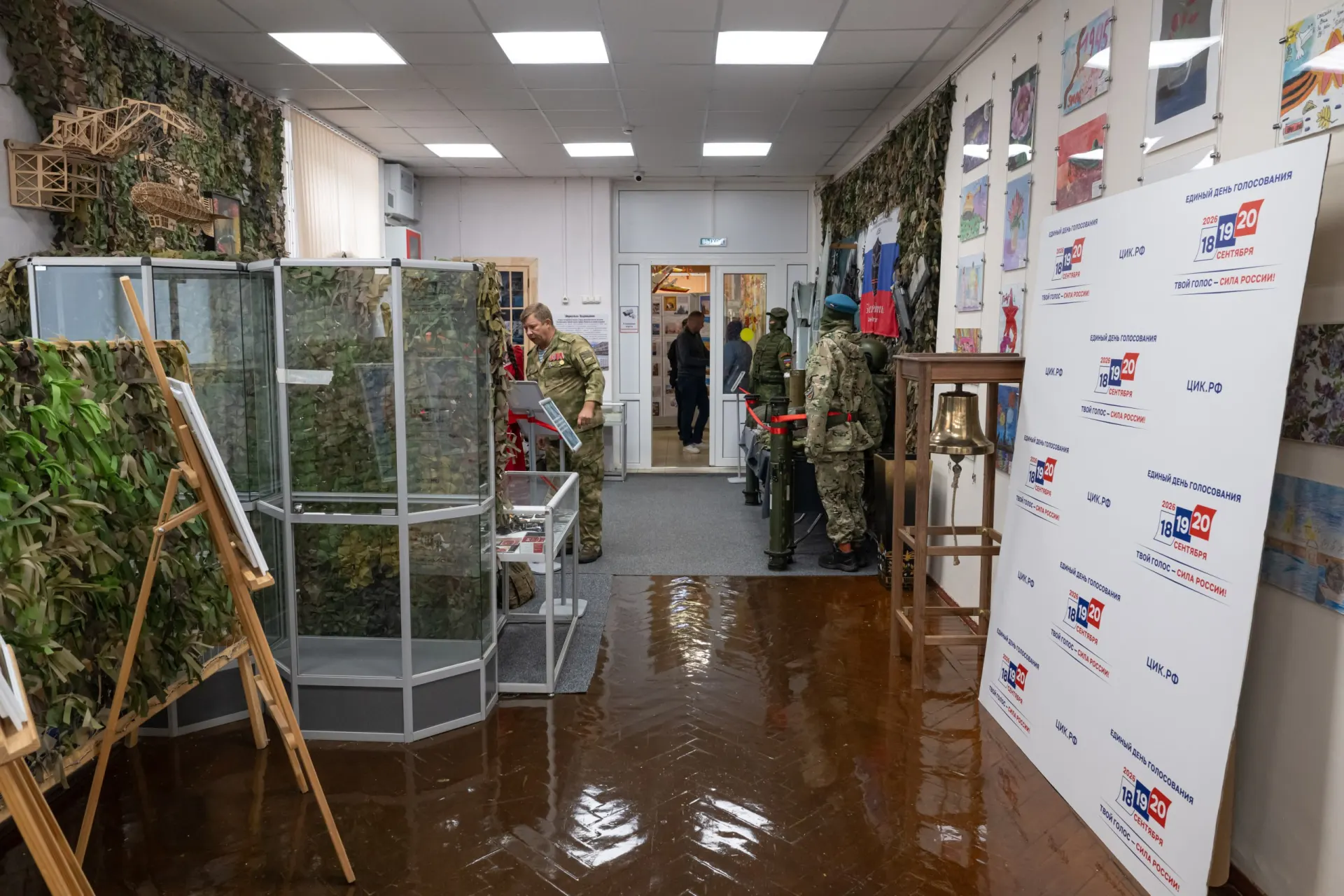 На фоне маскировки и военной формы проходят выборы; музейная экспозиция рассказывает о боевых днях, а посетители знакомятся с экспонатами и письмами; участие в голосовании принял участник войны.